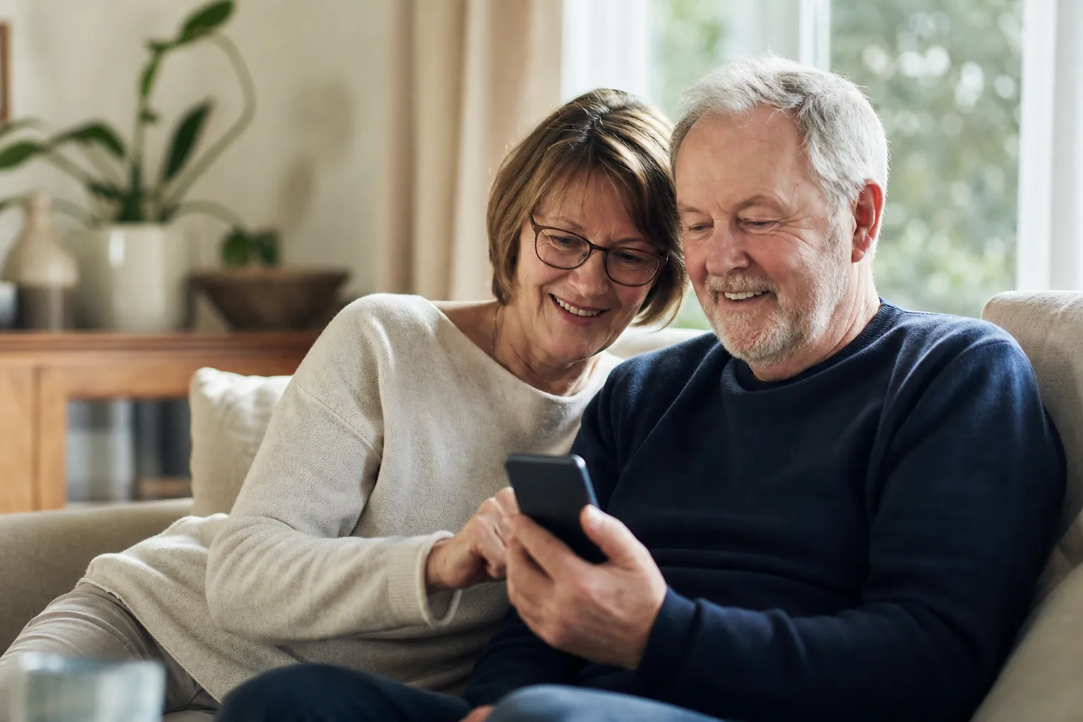 Äldre par vid köksbordet som tittar på en mobiltelefon tillsammans
